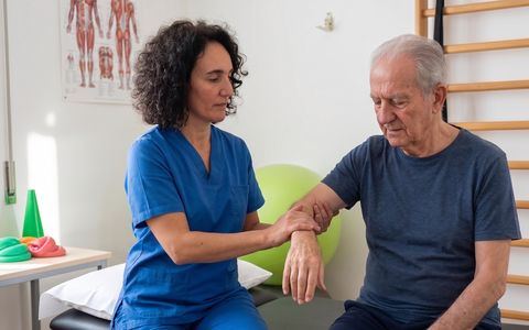 Fisioterapista assiste un paziente anziano durante una seduta di riabilitazione